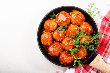 Meatballs with spicy tomato sauce in frying pan on white kitchen table. Top View