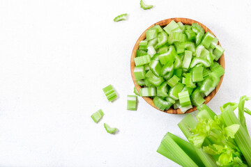 Chopped green celery in bowl, white table background, top view, copy space