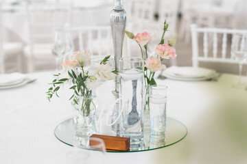 Close-up of a wedding dinner table at reception. Fresh flowers and candles on mirros plate. Wedding decorations.