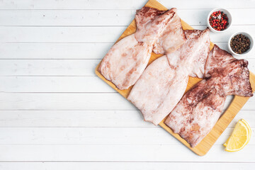 Raw squid carcass with spices and lemon ready for cooking on a wooden cutting board. copy space. Top view