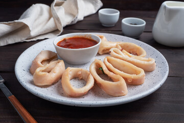 Fried squid rings with tomato sauce and lemon. Dark wooden background copy space.