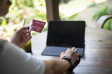 Asian woman sitting on the floor by the sofa, shopping online with laptop and entering credit card details for payment at home.