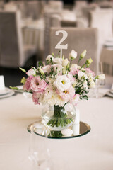 Centerpiece made of pink and white flowers stands in the middle of festive dinner table.