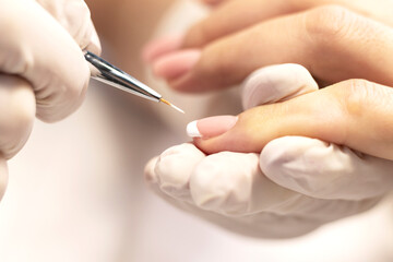 Obraz na płótnie Canvas French manicure is the process of performing a procedure in a beauty salon by a manicure master. White gel polish and a fine brush. Close-up