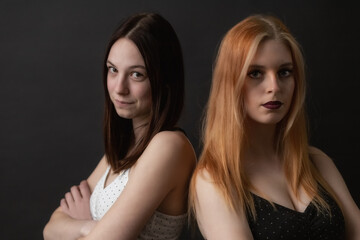 Couple of young women is posing on the black background. Horizontally. 