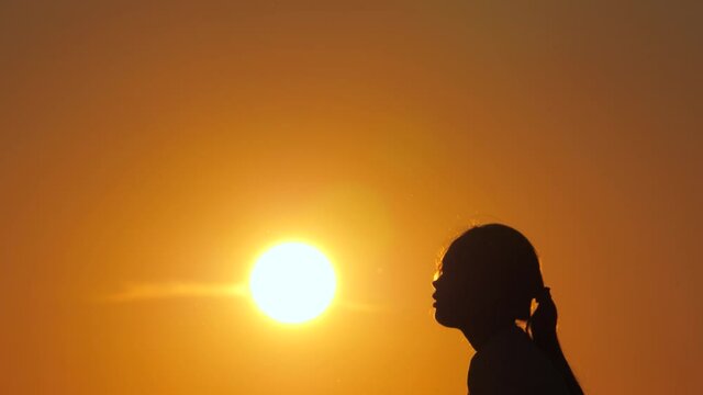 Silhouette of a child throwing ball with his hands up at sunset. Girl plays volleyball in the park in sun. A happy family. Active lifestyle of children. Sports achievement. The path to dream. Football