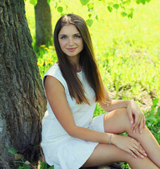 Portrait of beautiful young woman sitting on a grass in summer park