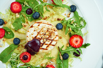 Grilled camembert cheese with apples, strawberries and blueberries in a white plate on a white plate. Close up, selective focus