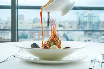 Appetizing red Bouillabaisse soup is poured from a bowl with salmon, scallop, langoustines and...