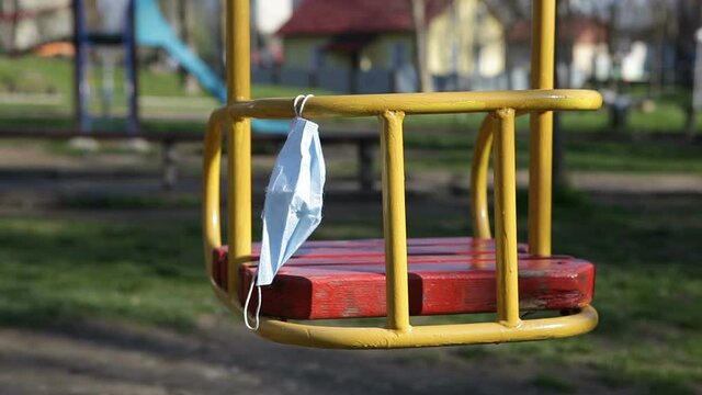 A medical mask hangs on a swing in an empty city park. Deserted playground. Coronavirus restrictions. A ban on visiting parks and squares. Coronavirus, May 2021.
