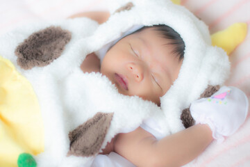 An Asian baby girl in a white cow costume is sleeping on a mattress.