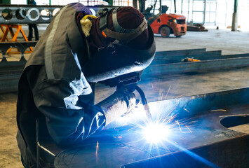 Craftsman welding steel structure with sparks fly from gas in fabrication factory.