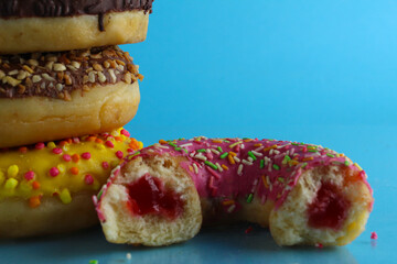 Yellow pink chocolate donuts lie a stack of a row of cut-off bitten doughnut stuffed with pink chocolate on a blue bright background with room for text. still life from food