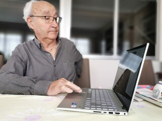 Elderly man sit on couch at home talk on video call on laptop with family friends, senior grandfather relax on sofa in living room speak communicate online use Webcam conversation