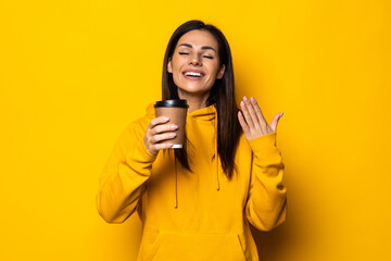 Beautiful woman holding a cup of coffee on yellow background