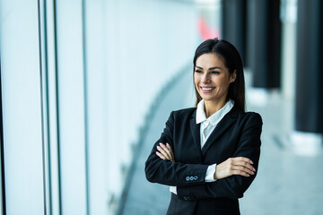 Businesswoman with crossed hands portrait in office with panormic windows.