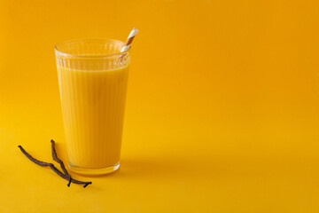 Delicious vanilla milkshake in glass on yellow background. Copy space