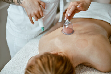 Obraz na płótnie Canvas professional female specialist is doing cupping therapy on the back of beautiful caucasian lady