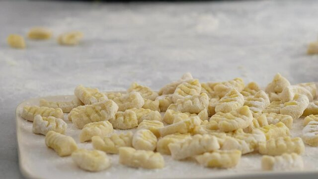 Woman making homemade pasta potato gnocchi. Dropping the dough onto the floured wooden surface into pieces.