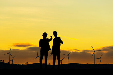 Fototapeta na wymiar Silhouette of Engineer and worker with clipping path in hard hat checking project at wind farm site on sunset in evening time