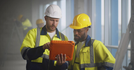 Diverse builders inside house being renovated using digital tablet