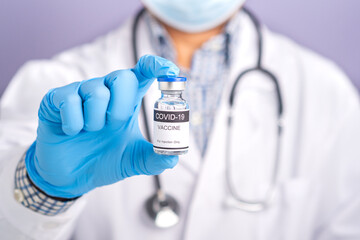 Doctor with a stethoscope on the shoulder wearing a face mask and holding a COVID-19 vaccine bottle. Vaccine for immunization, and treatment from coronavirus infection. Medical concept