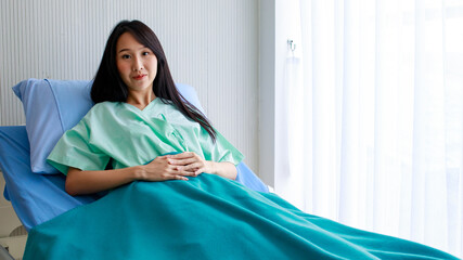 Young Asian lady patient lay down on blue bed green blanket white room in hospital. Look at camera...