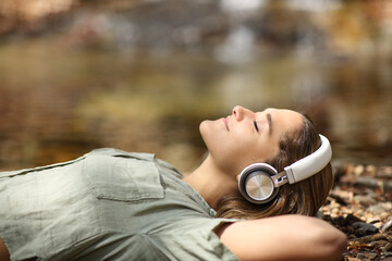 Woman listening to music lying in a riverside