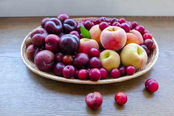 peach, plum and cherry plum in a wooden basket on table.