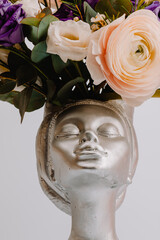 Woman face in the shape of a vase for flowers with Anemone eustoma ranunculus.