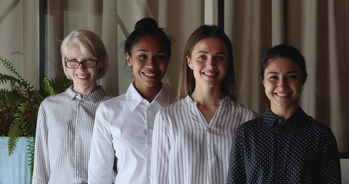 Confident happy older and young mixed race business women posing together in modern office room, smiling interracial diverse professional international different generations team looking at camera.