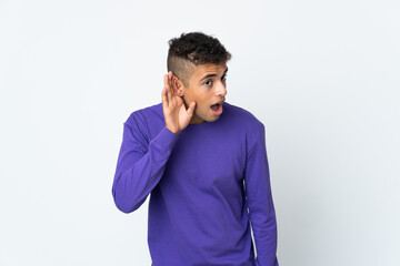 Young brazilian man isolated on white background listening to something by putting hand on the ear