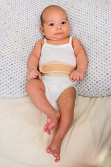 Baby in an umbilical hernia bandage. Sweet infant on the bed