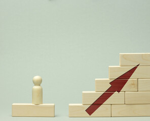 wooden figurine of a man stands on a staircase made of blocks on the first step. The concept of achieving the set goals in business, career growth