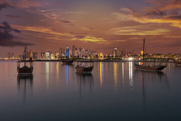 Fototapeta na wymiar Doha Qatar skyline at dusk showing skyscrapers lights reflected in the Arabic gulf and dhows in foreground with clouds in the sky in background