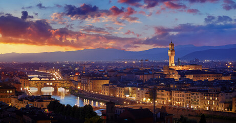 Fototapeta na wymiar Florence, Italy. Sunset panorama. Evening view at ancient city and famous Ponte Vecchio bridge on river Arno with picturesque clouds on sky and Bell tower on the horizon.