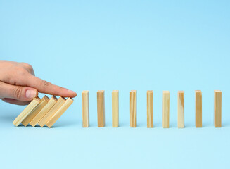 hand with a finger stops the fall of wooden bars on a blue background