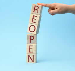 a hand with a finger holds a stack of wooden cubes on the reopen inscriptions