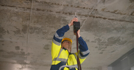 Construction worker drilling hole on ceiling with electrical drilling machine.