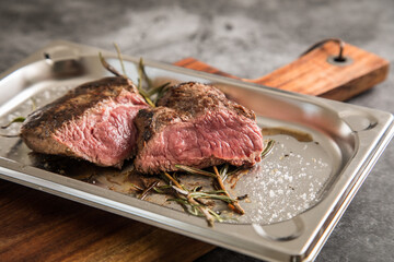 Rinder Steak medium rare gebraten mit Rosmarin und Salz auf Edelstahl Schale und Holzbrett und Stein Hintergrund dunkel