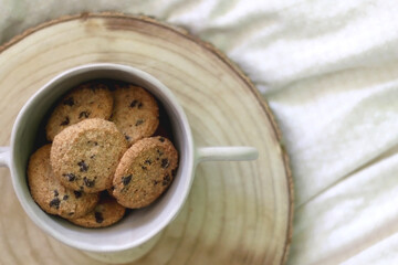 Bowl of chocolate chip cookies and wooden tray on a bed. Flat lay.