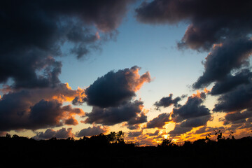 Naklejka premium Dramatic sunset with dark heavy clouds framing the blue and orange sky over silhouette of countryside agricultural field