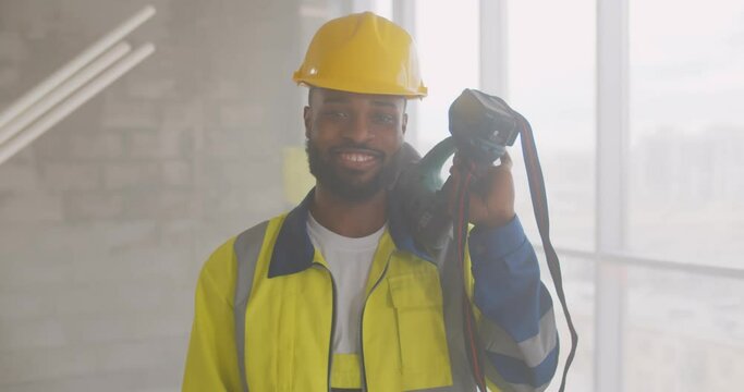Portrait of smiling afro-american builder in uniform holding drill on his shoulder