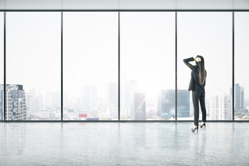 Fototapeta premium Businesswoman standing thinking in an empty big office room with big windows and city view. Real estate and future success concept
