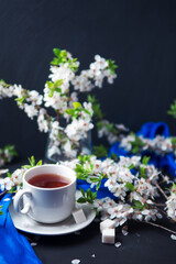 White Cup of hot tea, blooming branches of white cherry, blue delicate light spring scarf