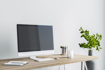 Modern computer monitor on wooden table with tea cup and notebook near stylish base on white wall background