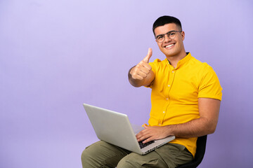 Young man sitting on a chair with laptop with thumbs up because something good has happened
