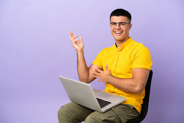 Young man sitting on a chair with laptop extending hands to the side for inviting to come