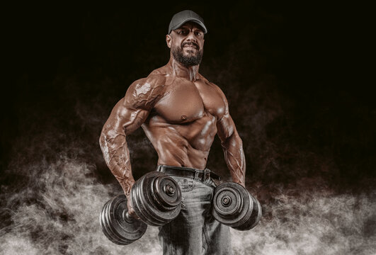 Muscular athlete posing in the studio with dumbbells. Fitness and classic bodybuilding concept.