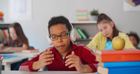 Portrait of preteen african kid in headphones rapping sitting at desk in classroom